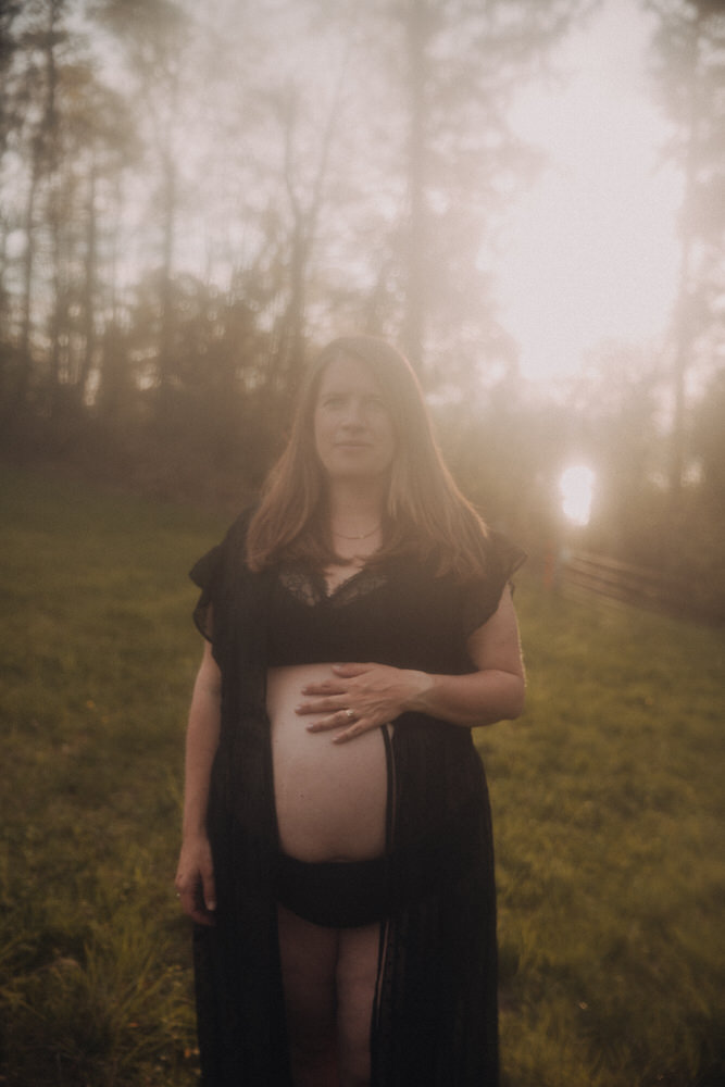 Schwangere Frau mit schwarzem Kimono vor Sonnenuntergang auf einer Wiese.