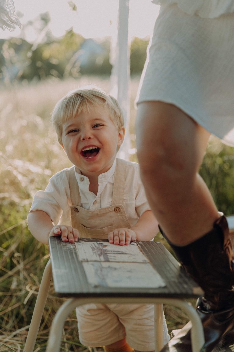 Natürliches Mama Kind Fotoshooting, Sohn hält sich an Trittleiter fest und lacht laut