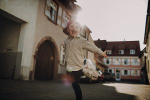 Familienfotoshooting in Altstadt mit untergehender Sonne. Sohn spielt Flieger und das Licht bricht von hinten warm durch