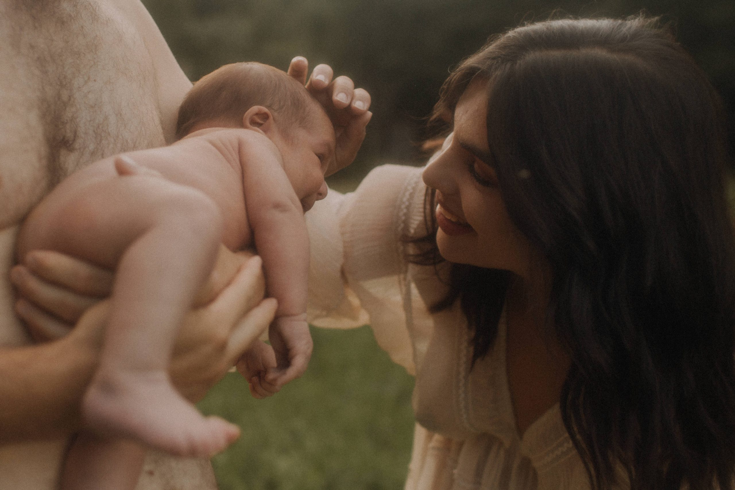 Newborn Fotoshooting in der Natur. Mama streichelt liebevoll über die Stirn des Babies.
