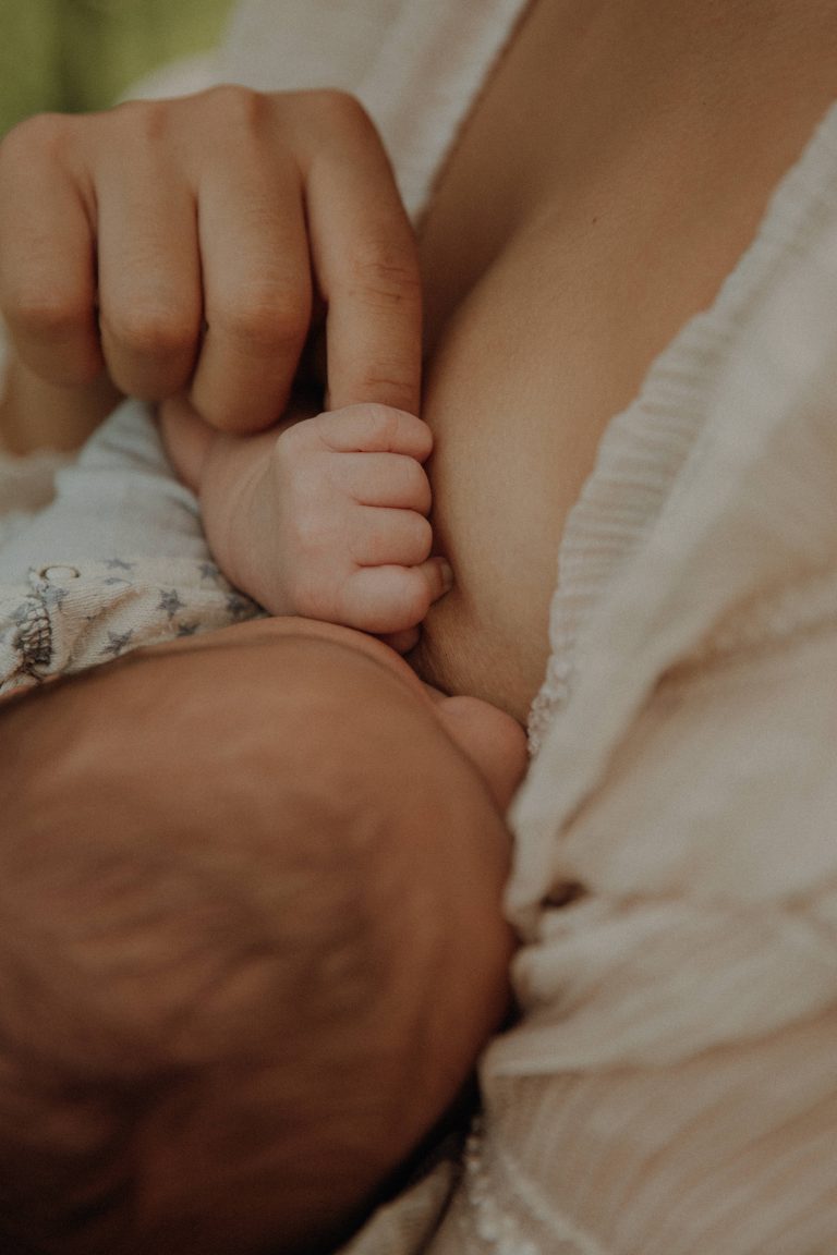 Neugeborenes Kind trinkt bei Mama an der Brust und hält ihren Finger fest.