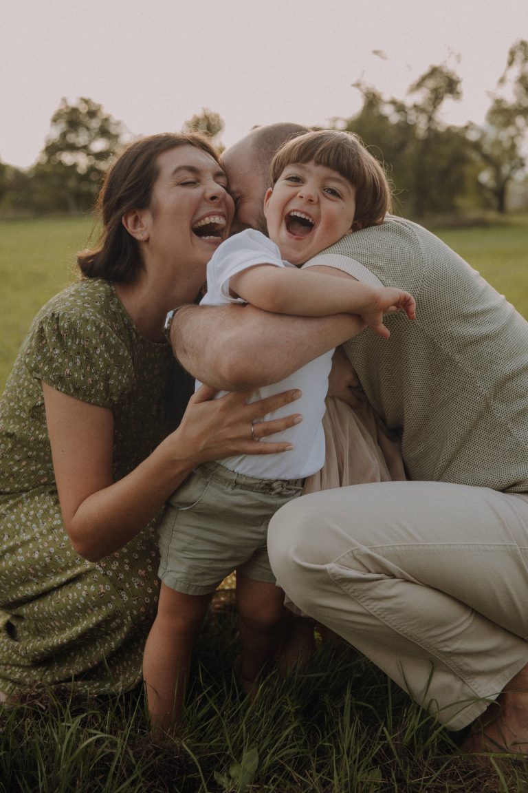 Eltern umarmen ihren laut lachenden Sohn auf einem Feld beim Familienfotoshooting