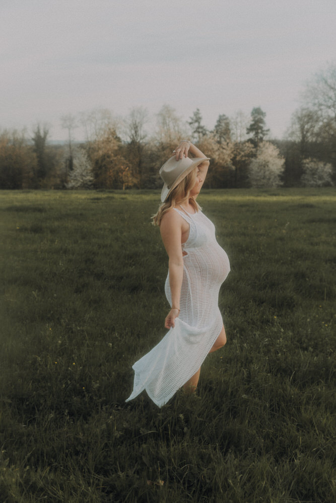 Frau mit Babybauch tanzt auf Feld mit engem Kleid