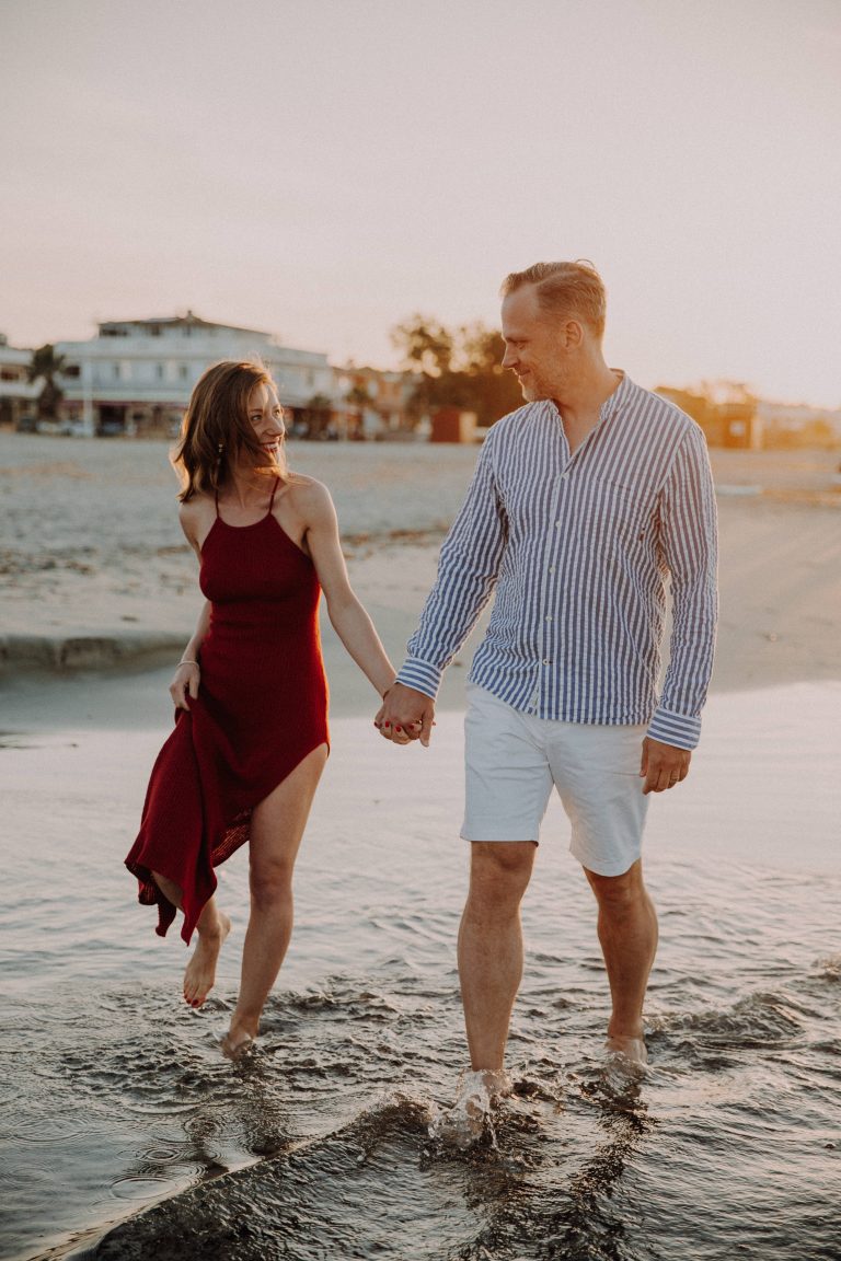 Paarshooting am Wasser bei Sonnenuntergang, Paar läuft locker und einander anlächelnd, barfuß im Wasser