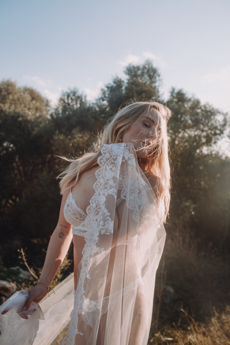 Boudoir Fine Art Shooting Outdoor – Frau in weißer Spitzeunterwäsche mit Spitzenschleier im Wind, mediterranes Gegenlicht