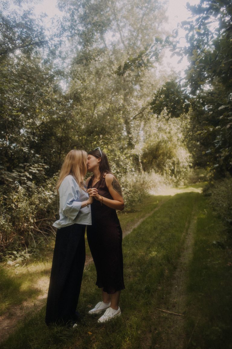 Romantisches LGBTQ Couple Shooting Outdoor – zwei Frauen küssen sich auf Waldweg in sommerlicher Natur
