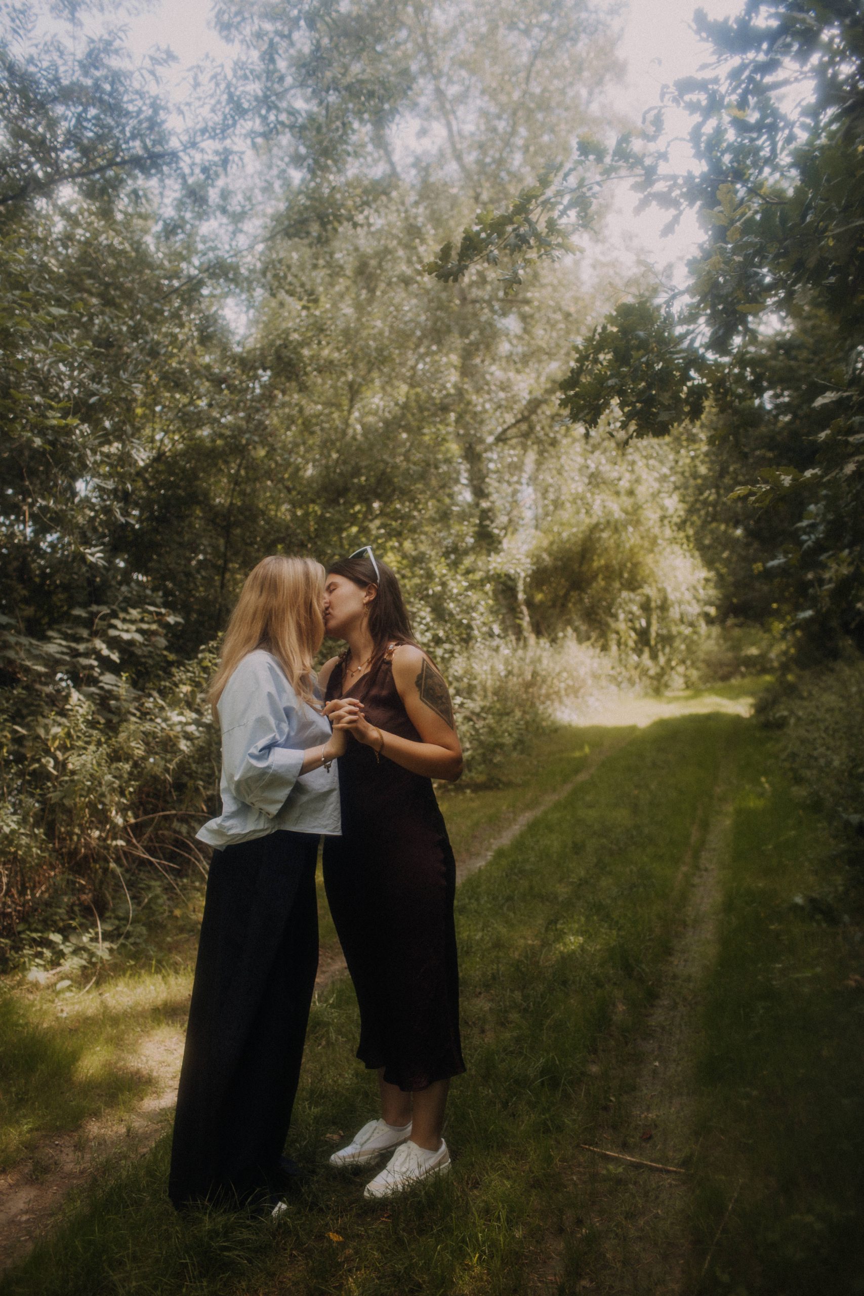 Romantisches LGBTQ Couple Shooting Outdoor – zwei Frauen küssen sich auf Waldweg in sommerlicher Natur
