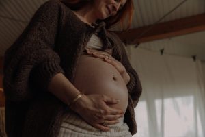 Schwangere Frau hält liebevoll ihren Babybauch mit beiden Händen – emotionales Babybauch Fotoshooting zu Hause