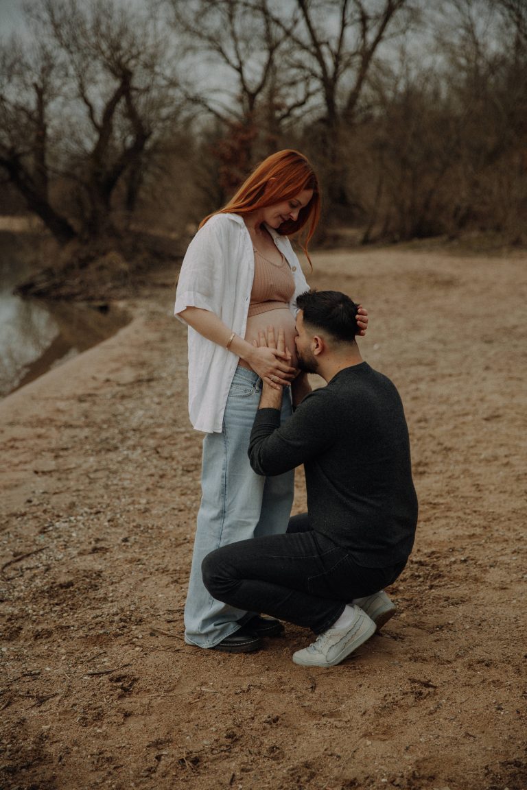 Emotionales Babybauch Fotohooting – Mann küsst den Babybauch seiner Partnerin am Seeufer
