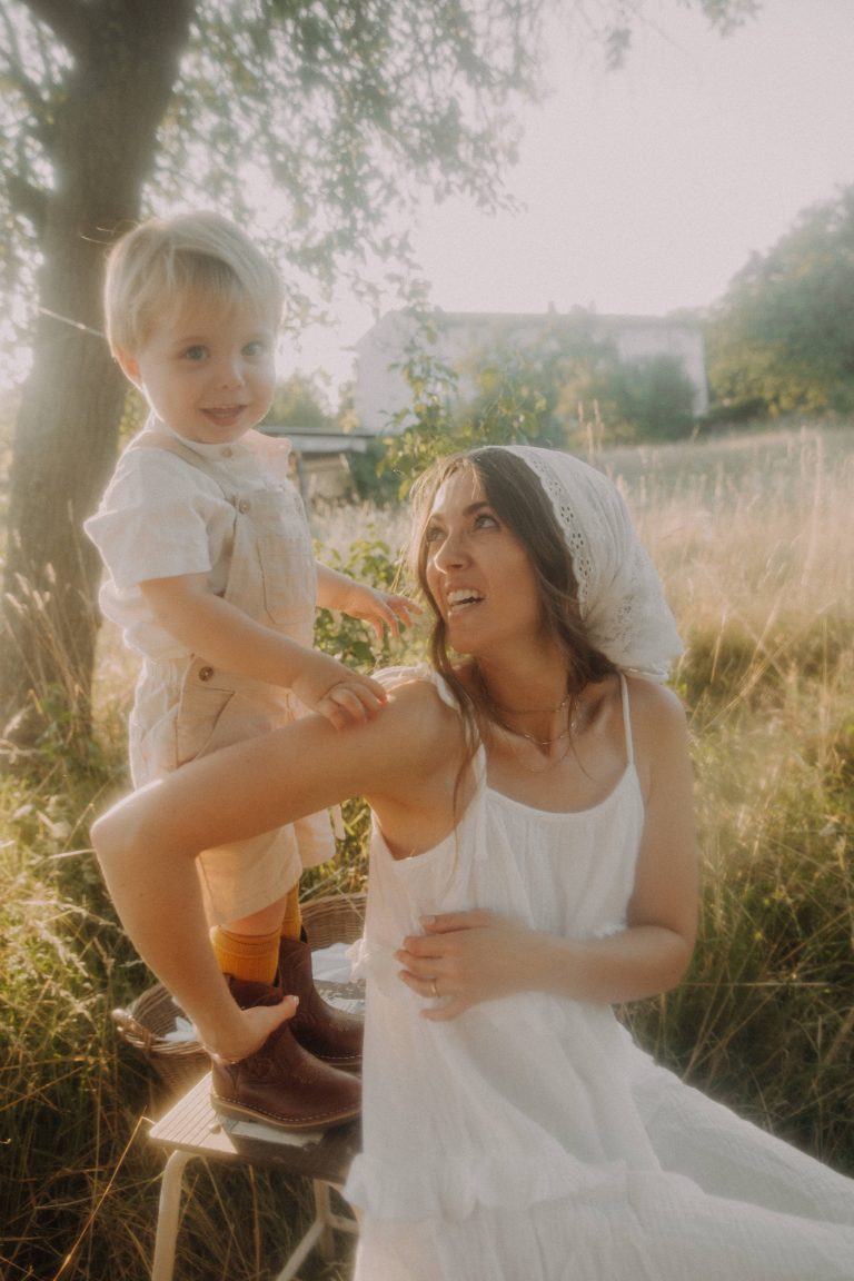 Mama und Kind Fotoshooting auf einem Feld. Sohn steht auf einem Tritthocker und die Mama dreht sich lachend zu ihm um.