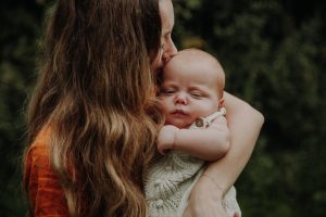Mutter küsst zärtlich ihr schlafendes Neugeborenes auf die Stirn – emotionales Newborn Fotoshooting im Freien