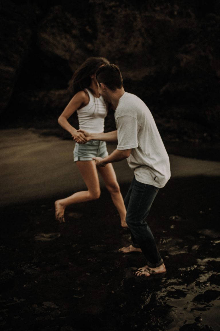 Authentisches Couple Shooting – Paar tanzt barfuß auf an dunklem Strand im stimmungsvollen Licht