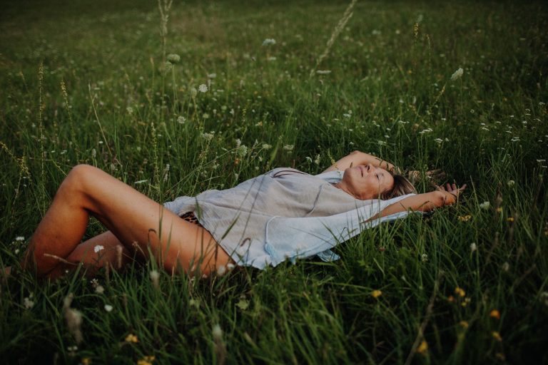 Leichtes Outdoor Boudoir Shooting – Frau liegt lächelnd in blühender Sommerwiese im warmen Abendlicht