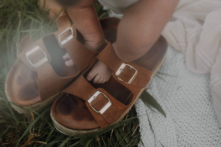 Newborn Fotografie Nahaufnahme. Babyfüße im Birkenstock Schuh der Schwester.