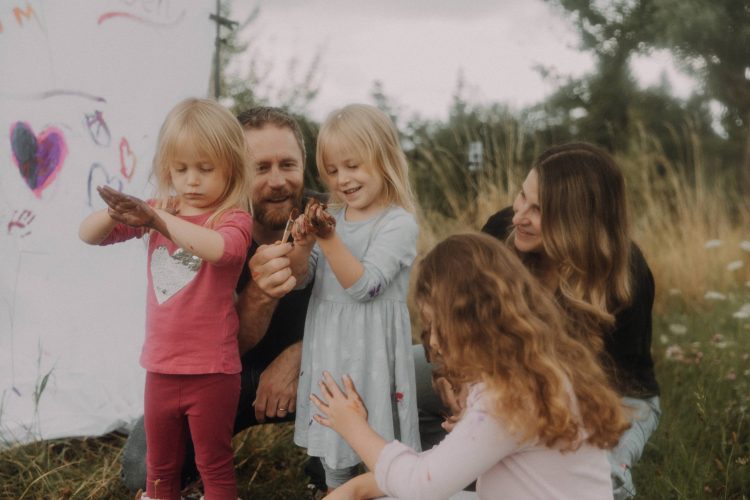 Familien Fotoshooting im Freien – Eltern und Kinder malen gemeinsam auf einer Leinwand im Grünen